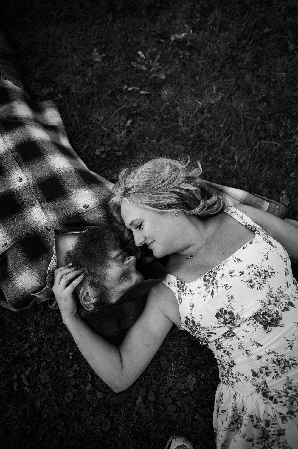 Black and white portrait of couple lying on grass wearing plaid and floral patterns.