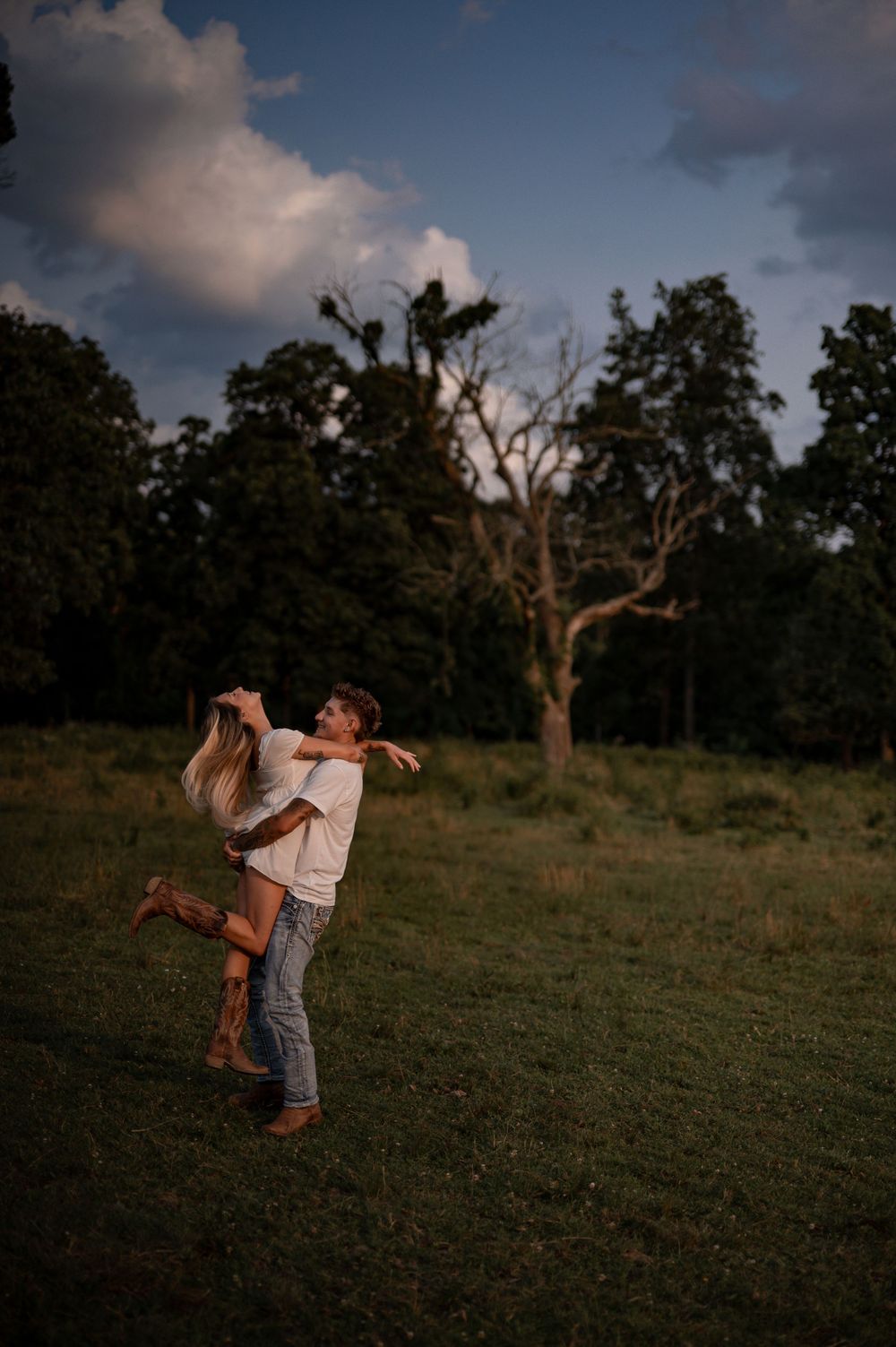 Couple shares a playful moment spinning in a grassy field at dusk.