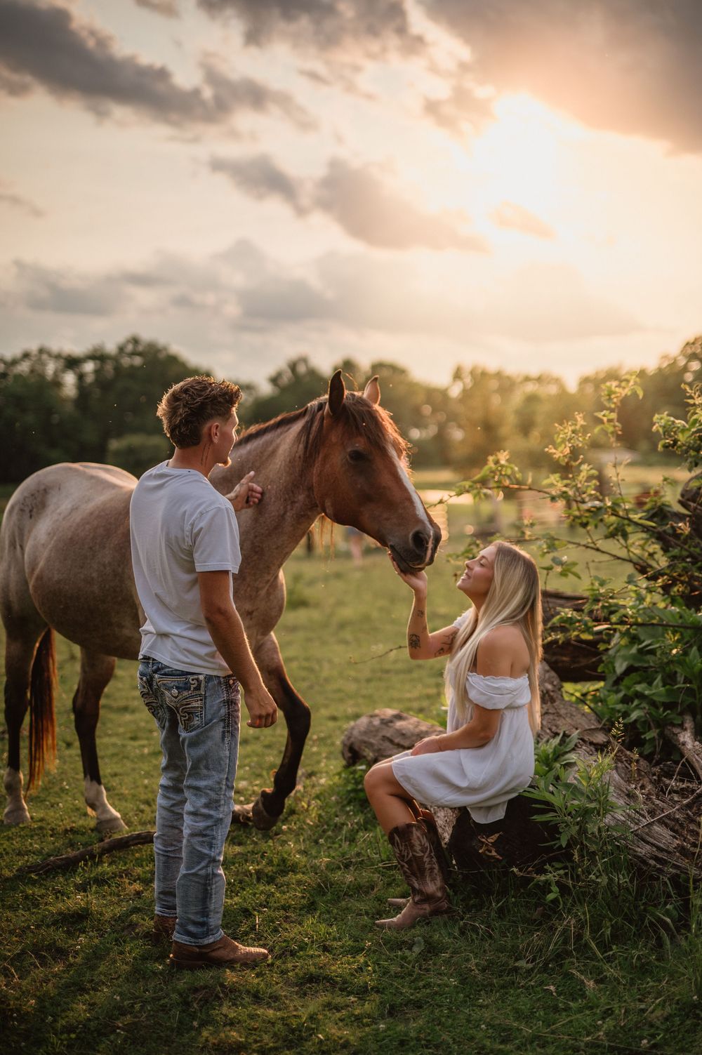 A couple interacts with a brown horse in a sunset-lit field during a photo session.