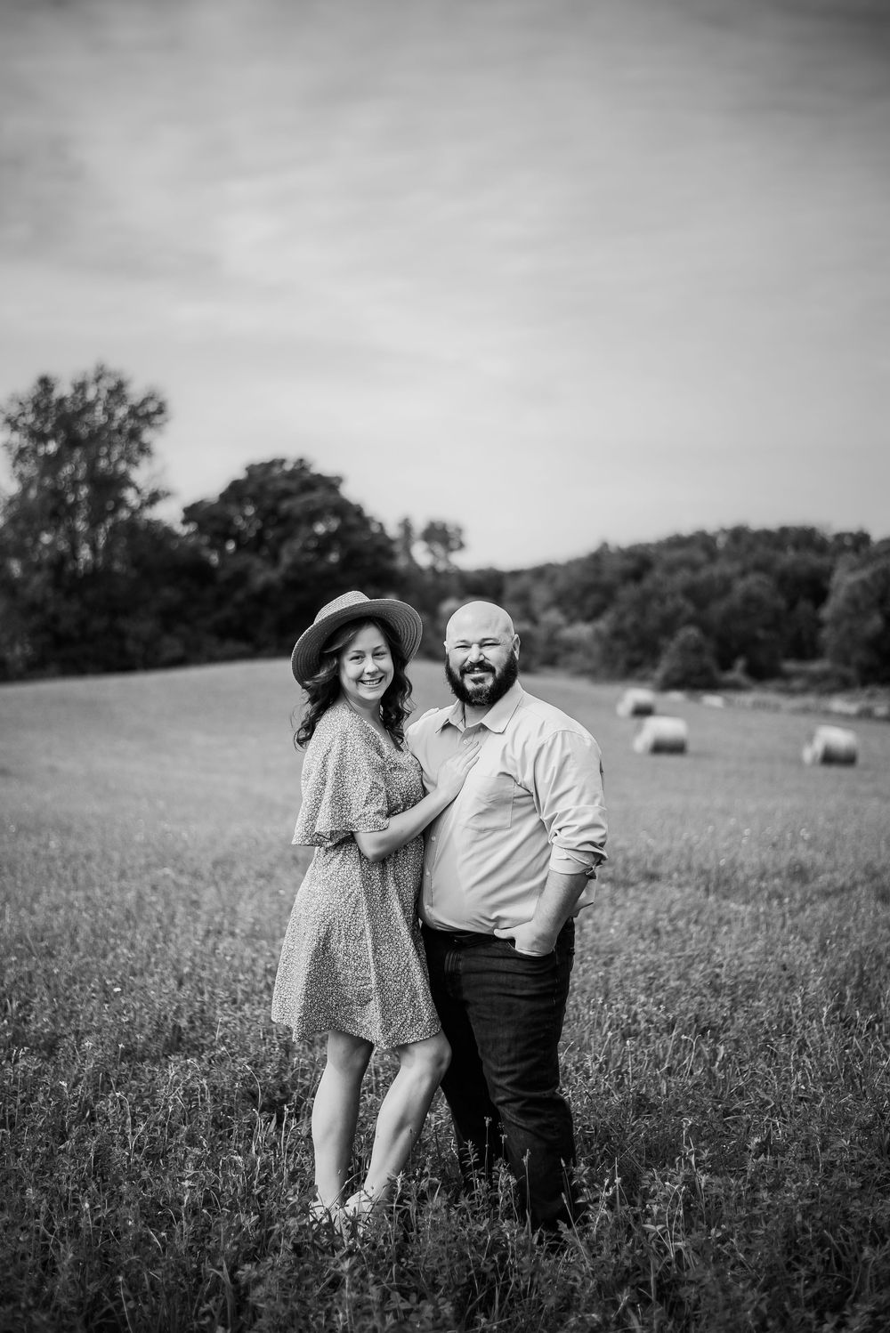 Black and white photo series of a couple embracing in a wildflower meadow with hay bales in the background.