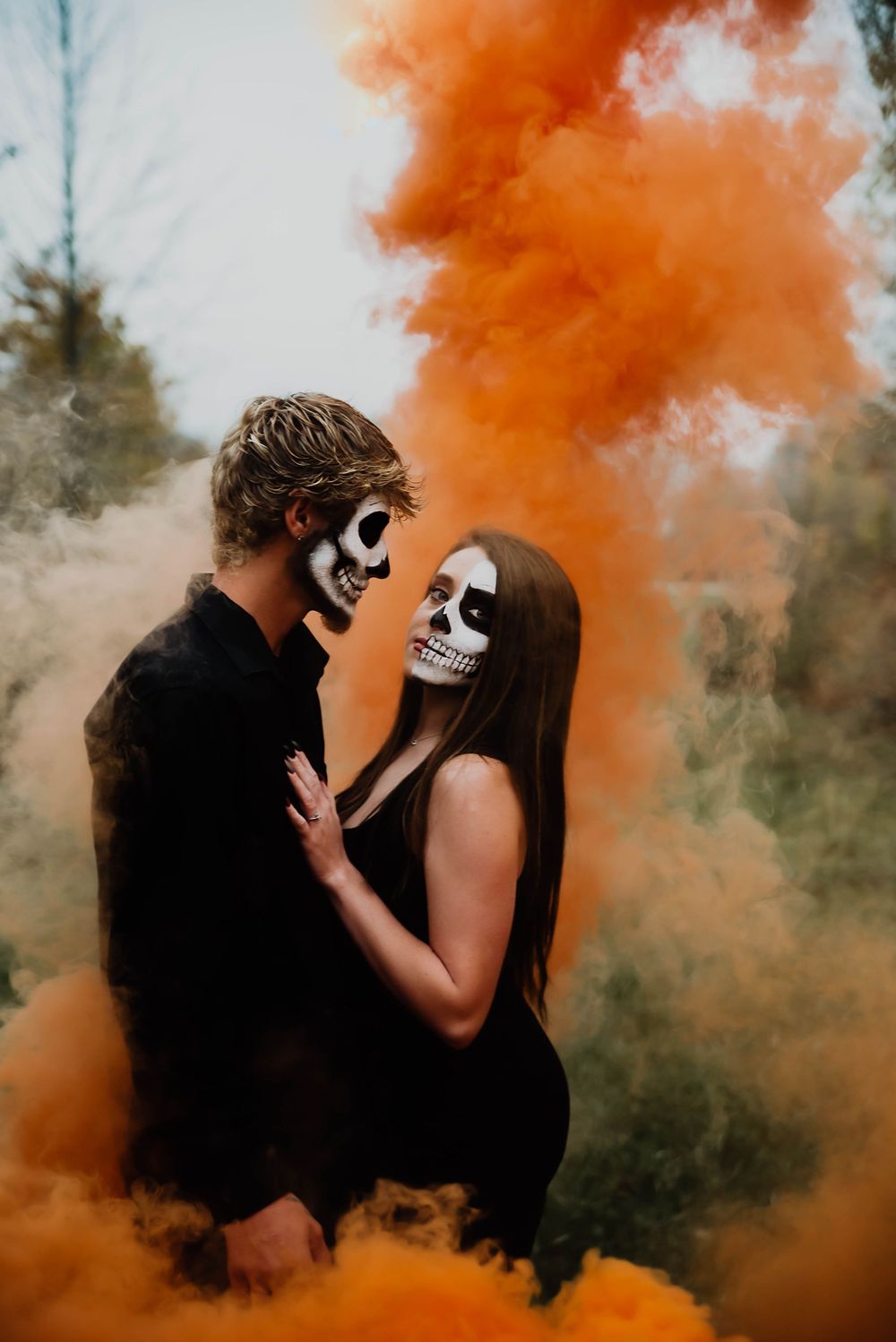 Dramatic couple photos with orange smoke bombs creating an ethereal Halloween atmosphere.