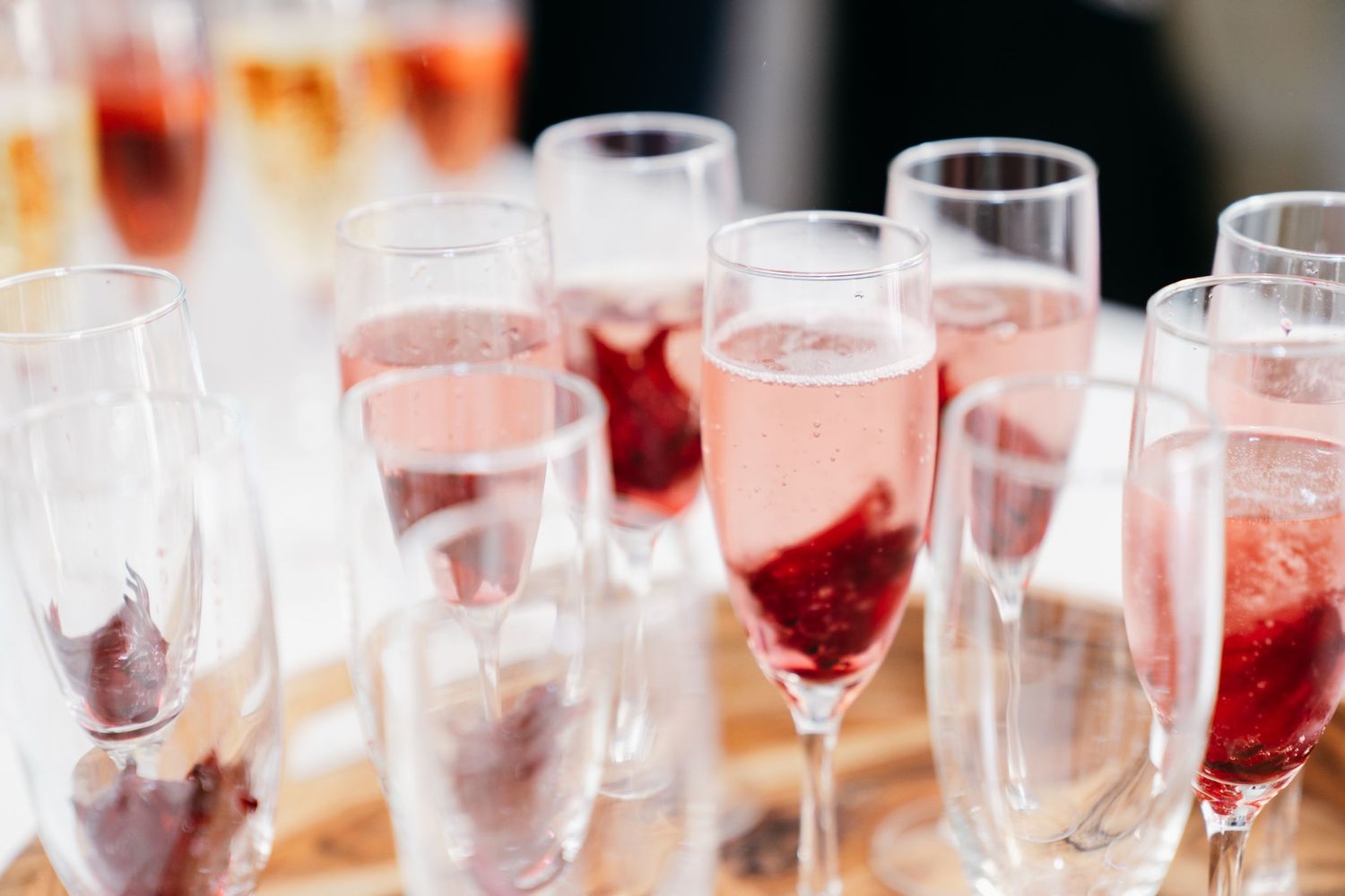Pink and red cocktails in elegant glasses lined up on a bar counter for a wedding celebration.