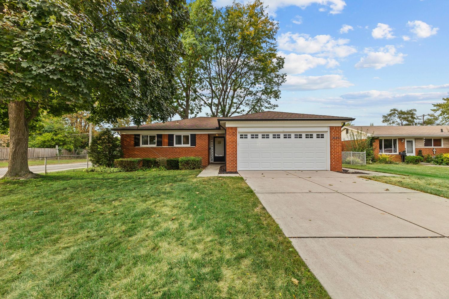Charming white clapboard bungalow with covered front porch, brick garage, and small front yard.