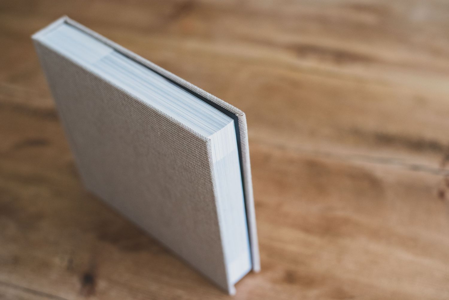 A minimalist hardcover book with linen texture cover resting on a wooden surface.