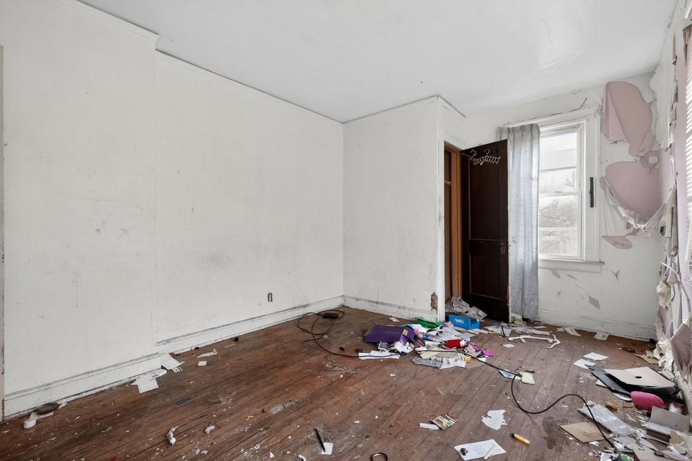 Abandoned room with peeling walls, scattered debris, and worn hardwood floors needing renovation. Detroit MI