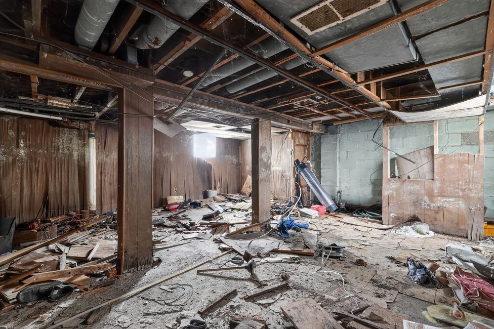 Abandoned building interior with debris-covered floor, exposed wooden beams, and deteriorating walls in a dilapidated structure. Detroit MI