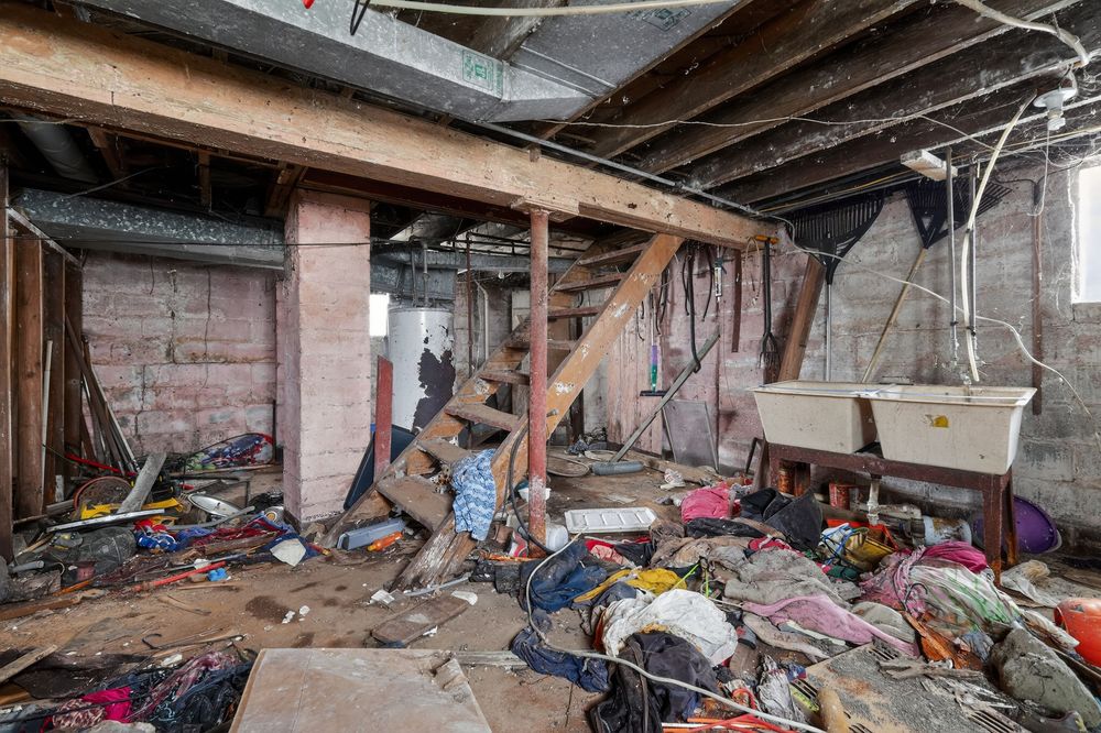 Demolished basement interior with debris, broken wood beams, brick columns, and scattered rubbish in an abandoned building. Detroit MI
