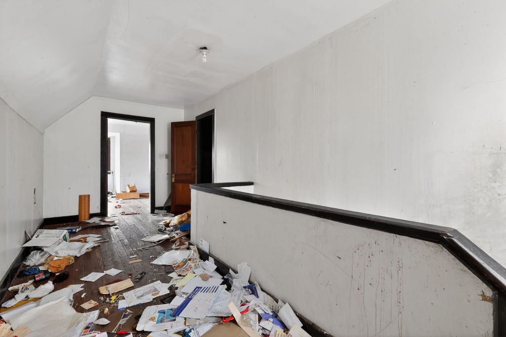 Abandoned hallway with debris and trash scattered on damaged hardwood floors in a neglected property. Detroit MI