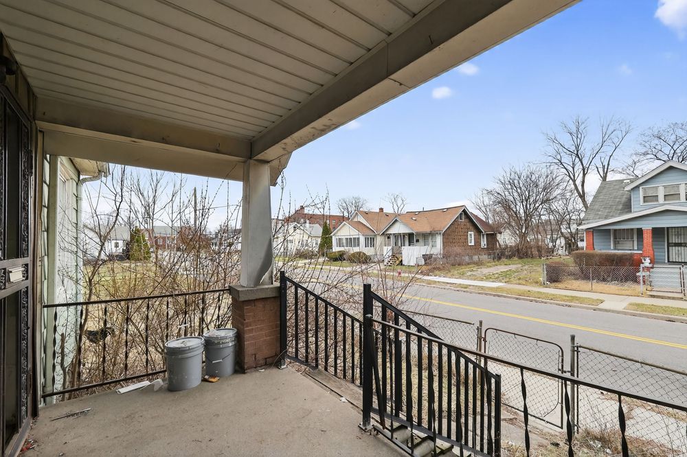 Covered front porch with black metal railing overlooking a quiet residential street with bare trees and neighboring homes. Detroit MI