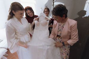 Bride and women examining elegant white wedding dress on hanger before ceremony.