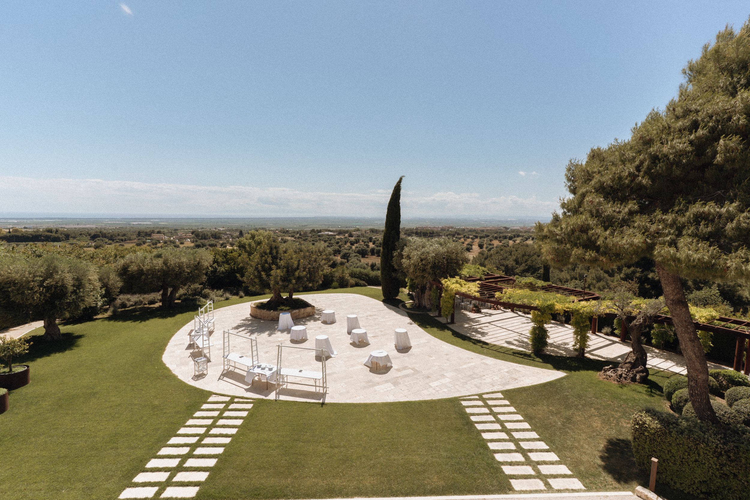 Aerial view of an elegant outdoor wedding venue with manicured gardens, stone pathways, and panoramic countryside views.