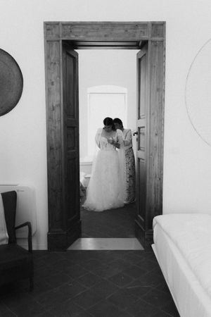 Black and white photo of a bride in a tulle gown being helped by a bridesmaid through a wooden doorway.