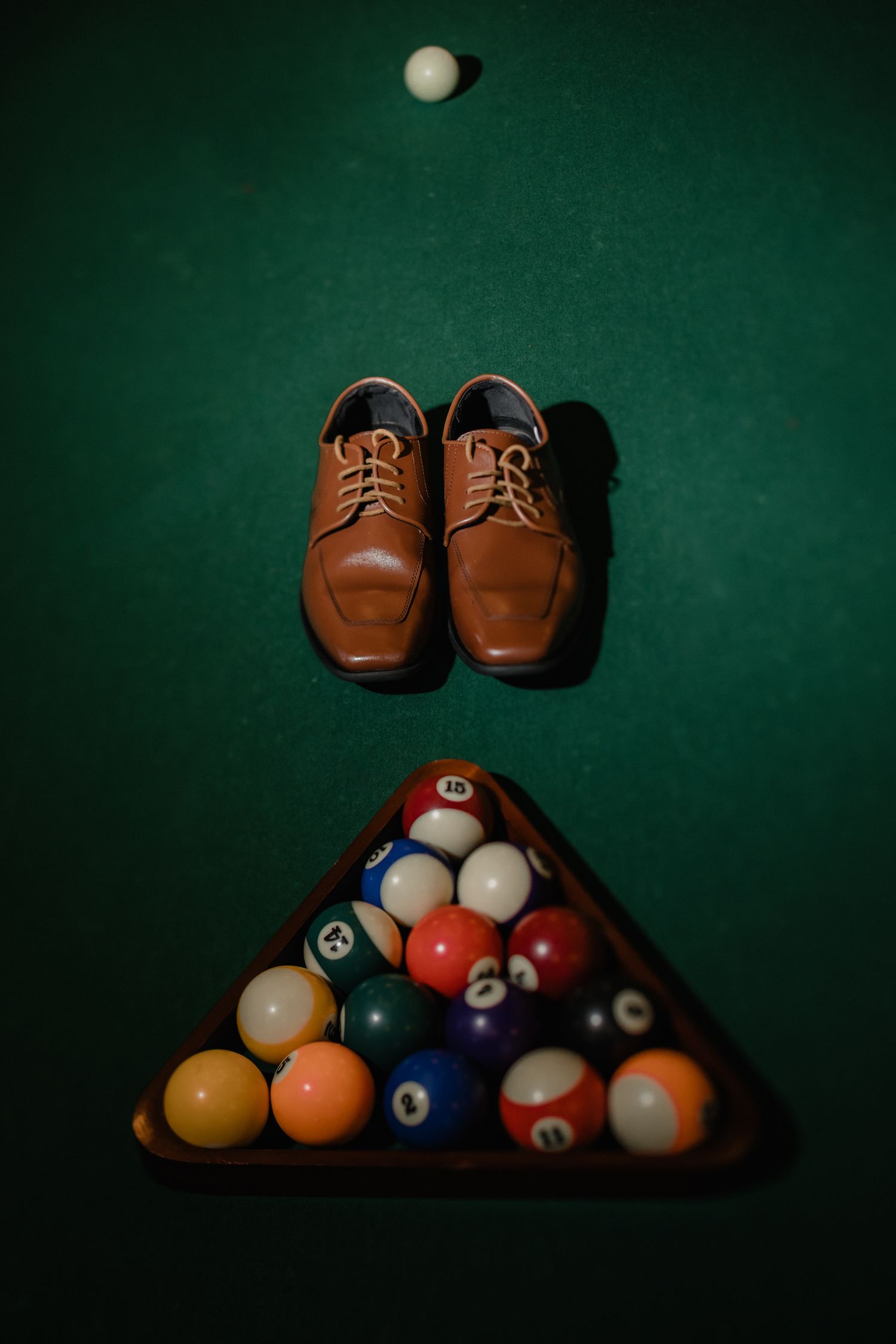 Brown leather dress shoes and racked billiard balls arranged on a green pool table for a wedding flat lay.