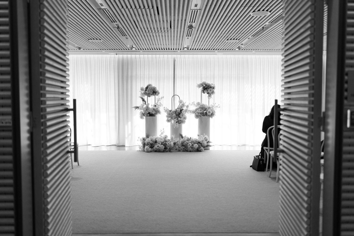 Black and white image of empty wedding ceremony space with floral arrangements and white drapes.