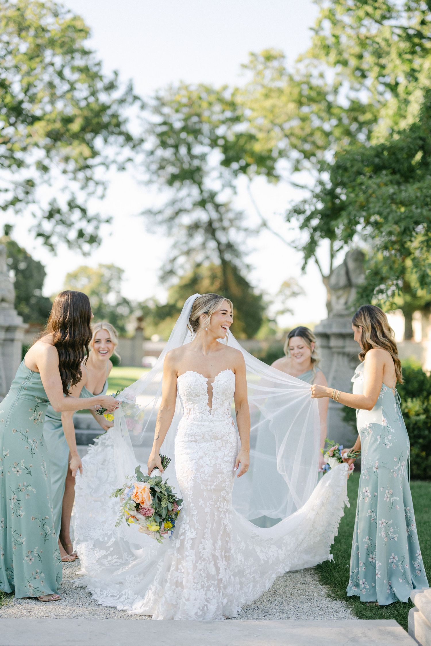 Armour House Wedding - Bride in lace gown with four bridesmaids in sage green dresses arranging her train in an elegant garden setting.