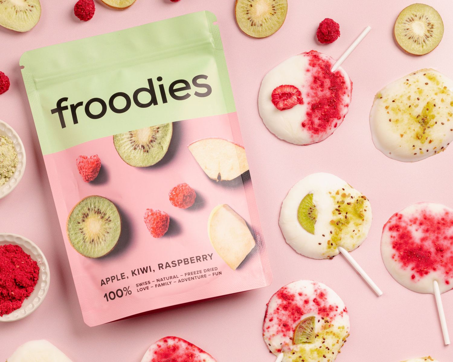 Overhead view of pink and green kiwi slices with raspberries and froodies packaging on pastel background.