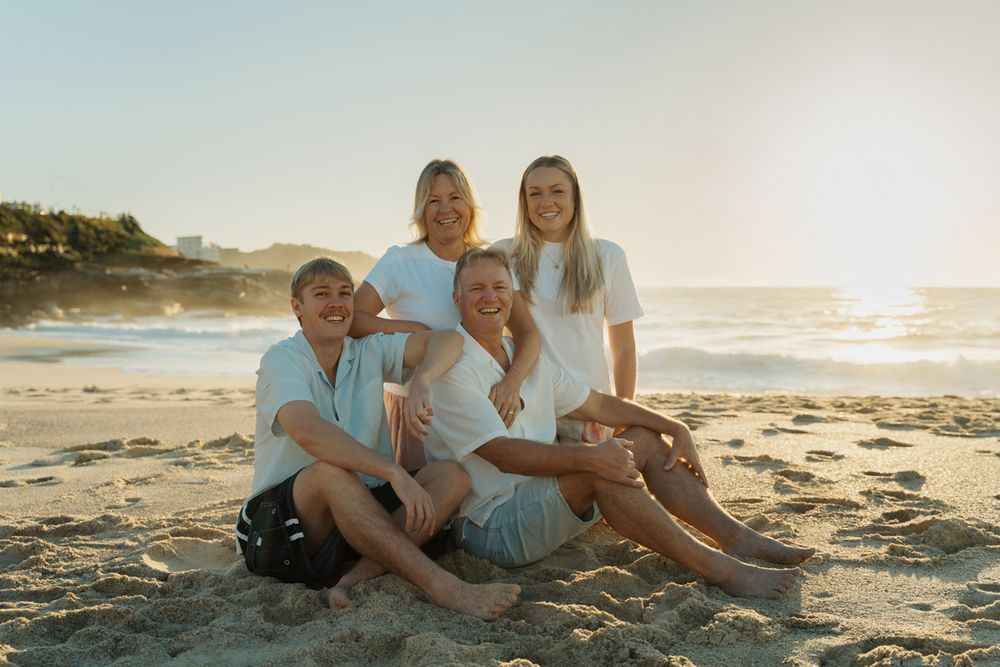 family of four smiling in white shirts sitting together on a sandy beach at Bronte at golden hour family photoshoot