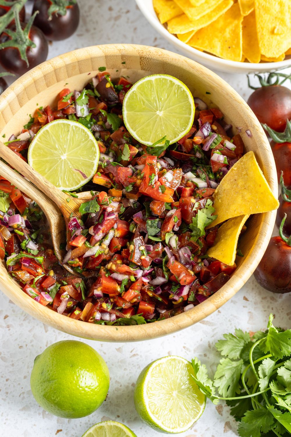 Fresh homemade pico de gallo salsa in wooden bowl with tortilla chips, lime slices, cilantro, and dark cherry tomatoes.