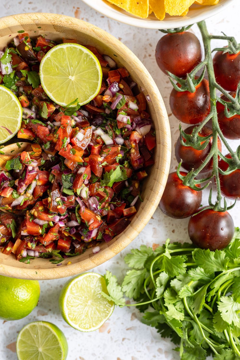 Fresh homemade pico de gallo salsa in wooden bowl with lime, cherry tomatoes, cilantro, and tortilla chips.