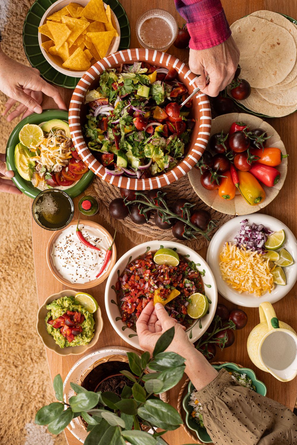 Overhead view of a vibrant Mexican taco spread with salad, guacamole, salsa, chips, and fresh toppings on a wooden table.