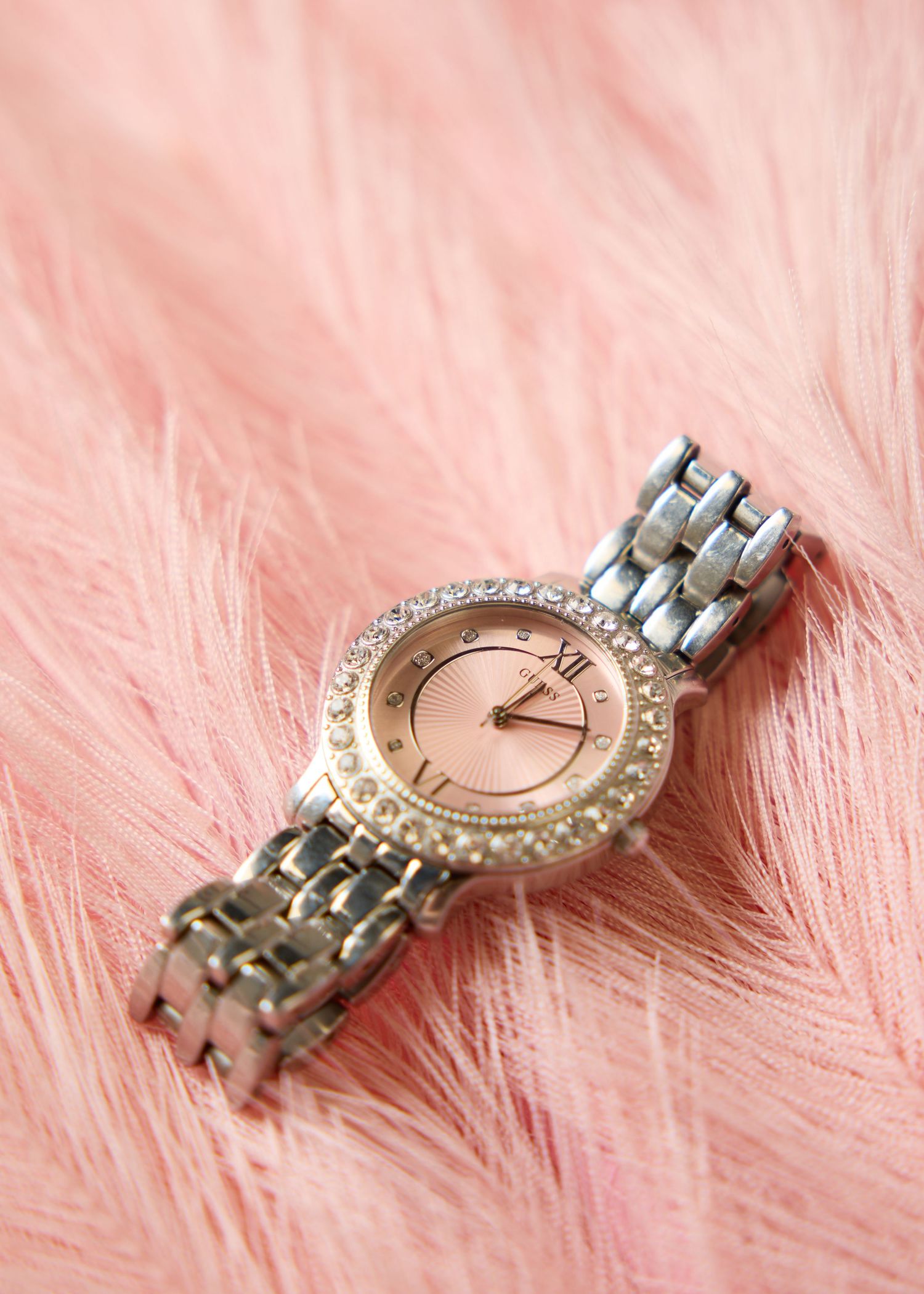 Silver and rose gold women's crystal-bezel bracelet watch on pink fur background.