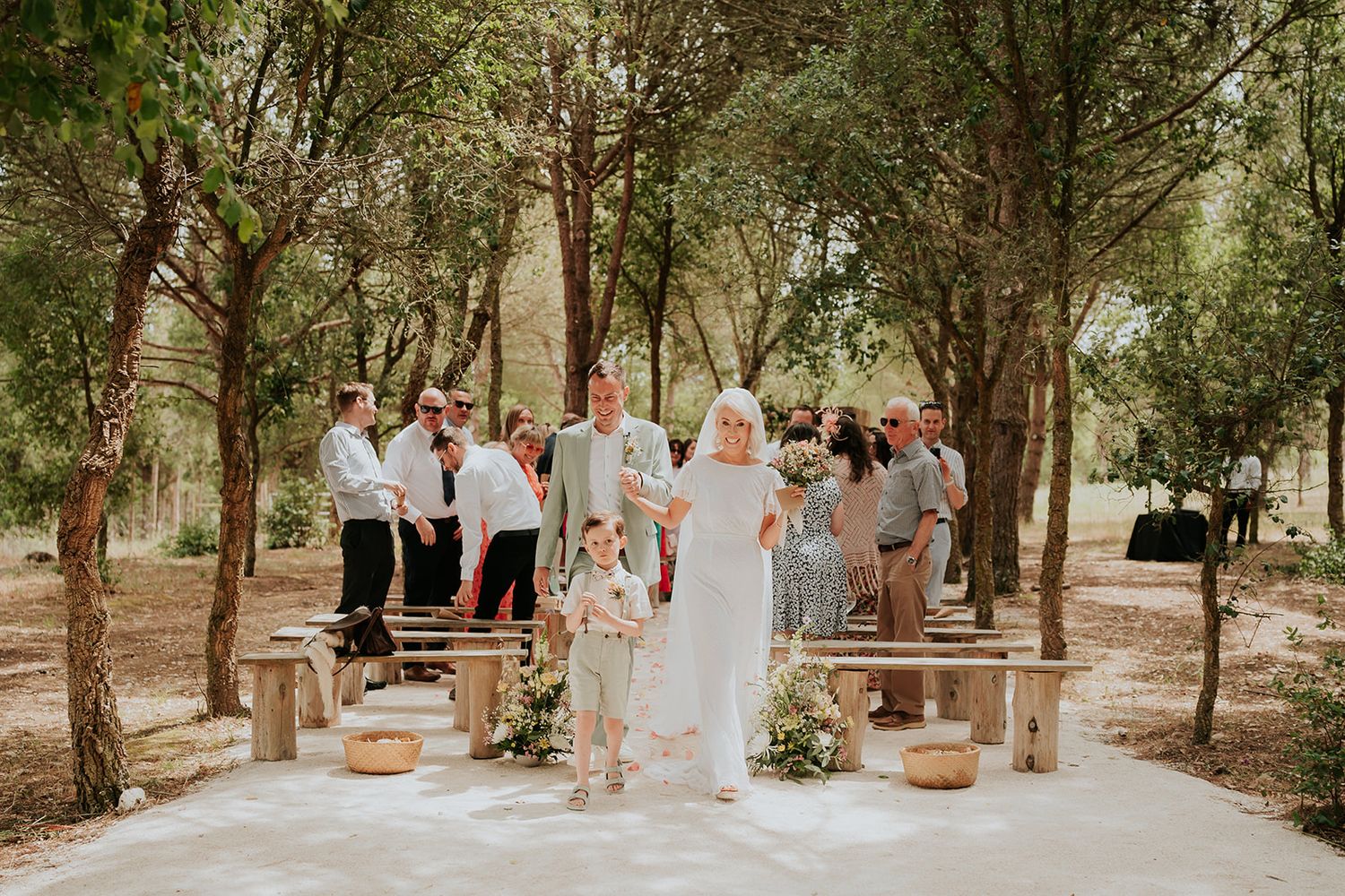 An outdoor wedding ceremony setup with wooden benches among a grove of tall trees.