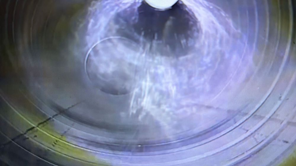 Close-up view inside a cylindrical tunnel with swirling water and mist creating a vortex pattern.