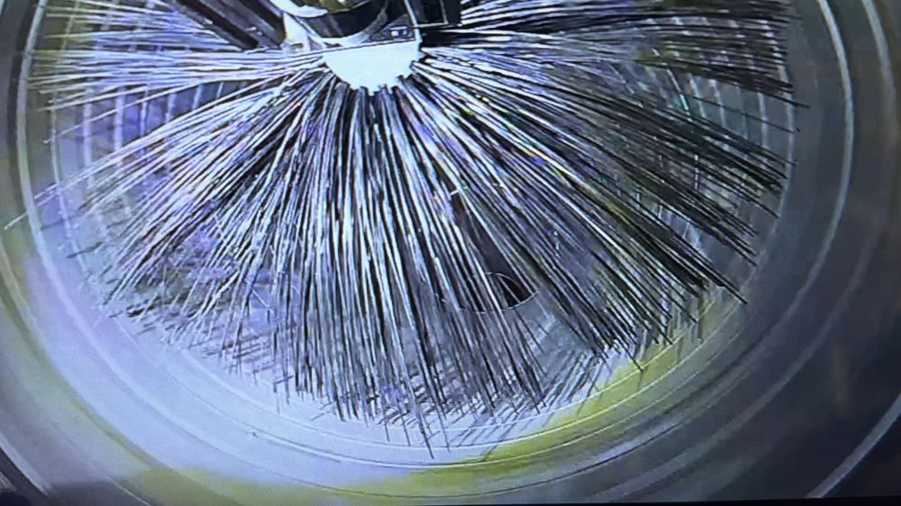 Close-up view of a rotating pipe cleaning brush with metal bristles inside a cylindrical pipe.