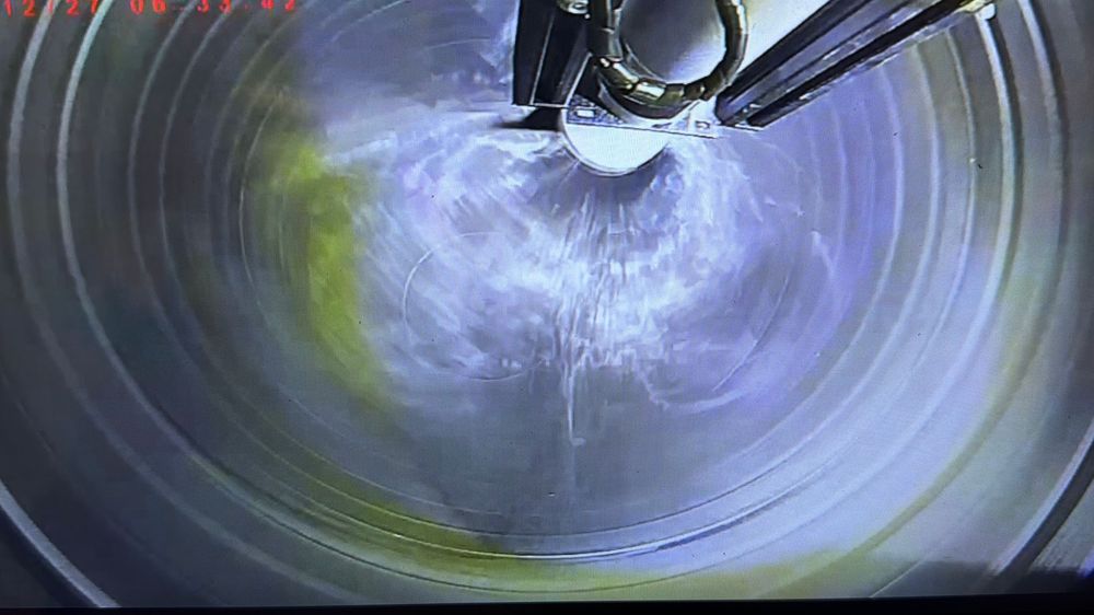High-pressure water jetting equipment cleaning the interior of an industrial pipe with yellow residue.