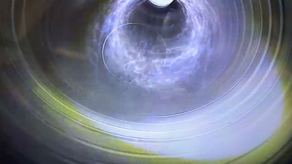 Interior CCTV inspection view of a clean cylindrical pipe with swirling light reflections on walls.