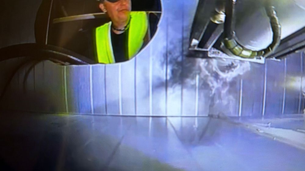 Worker in yellow vest inspects industrial tunnel with steam and blue lighting in high-tech facility.