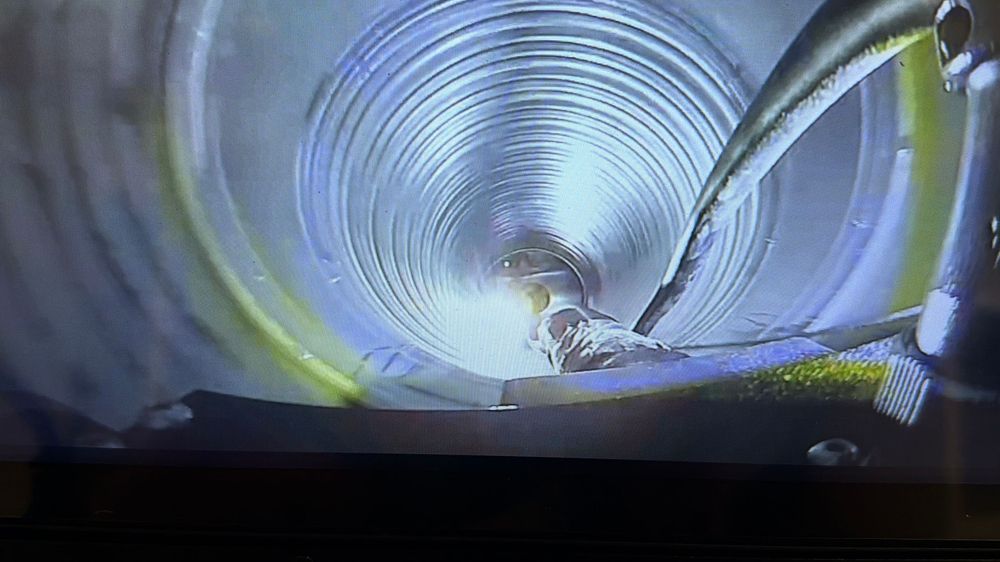 Worker performing welding inside a large industrial tunnel or pipe, illuminated by bright blue light.