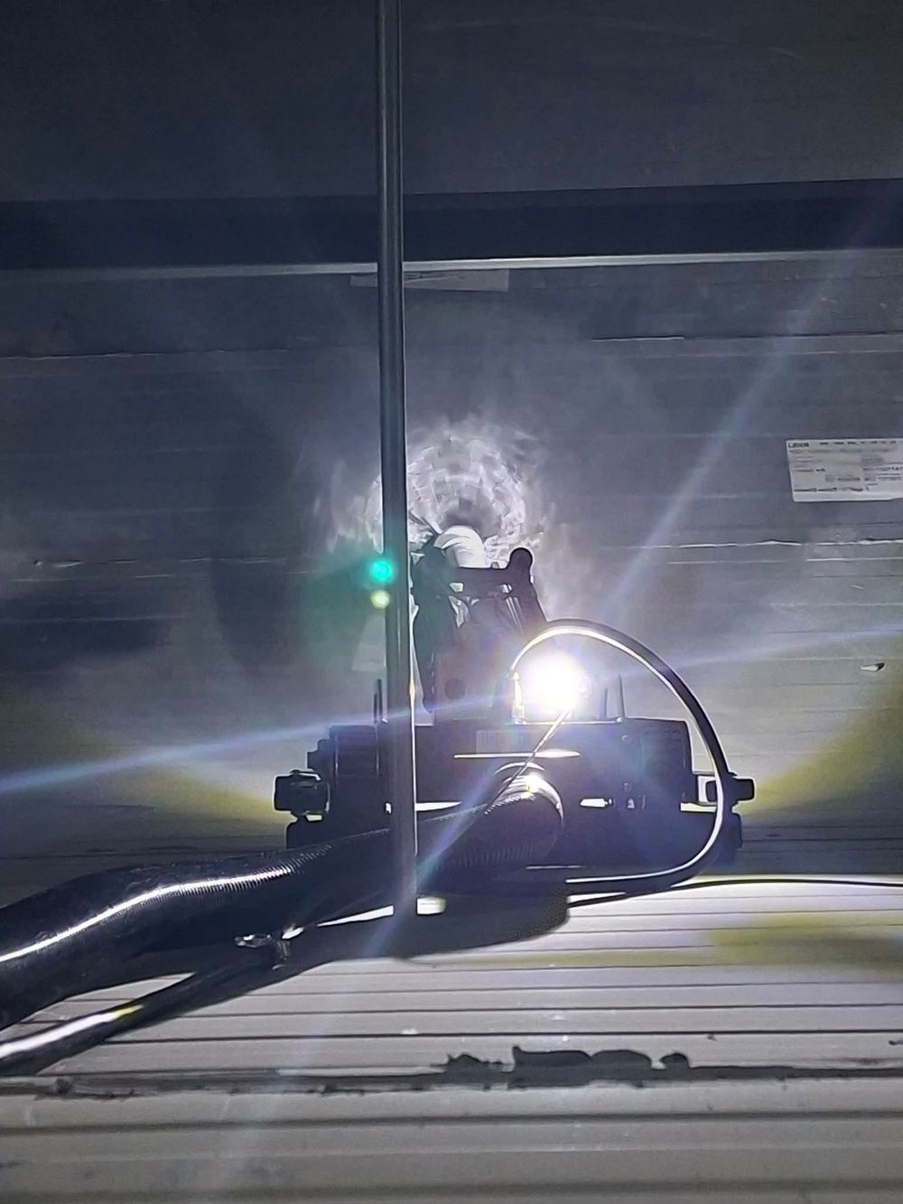 Welder working with bright light and smoke in dark industrial setting, performing arc welding on metal surface.