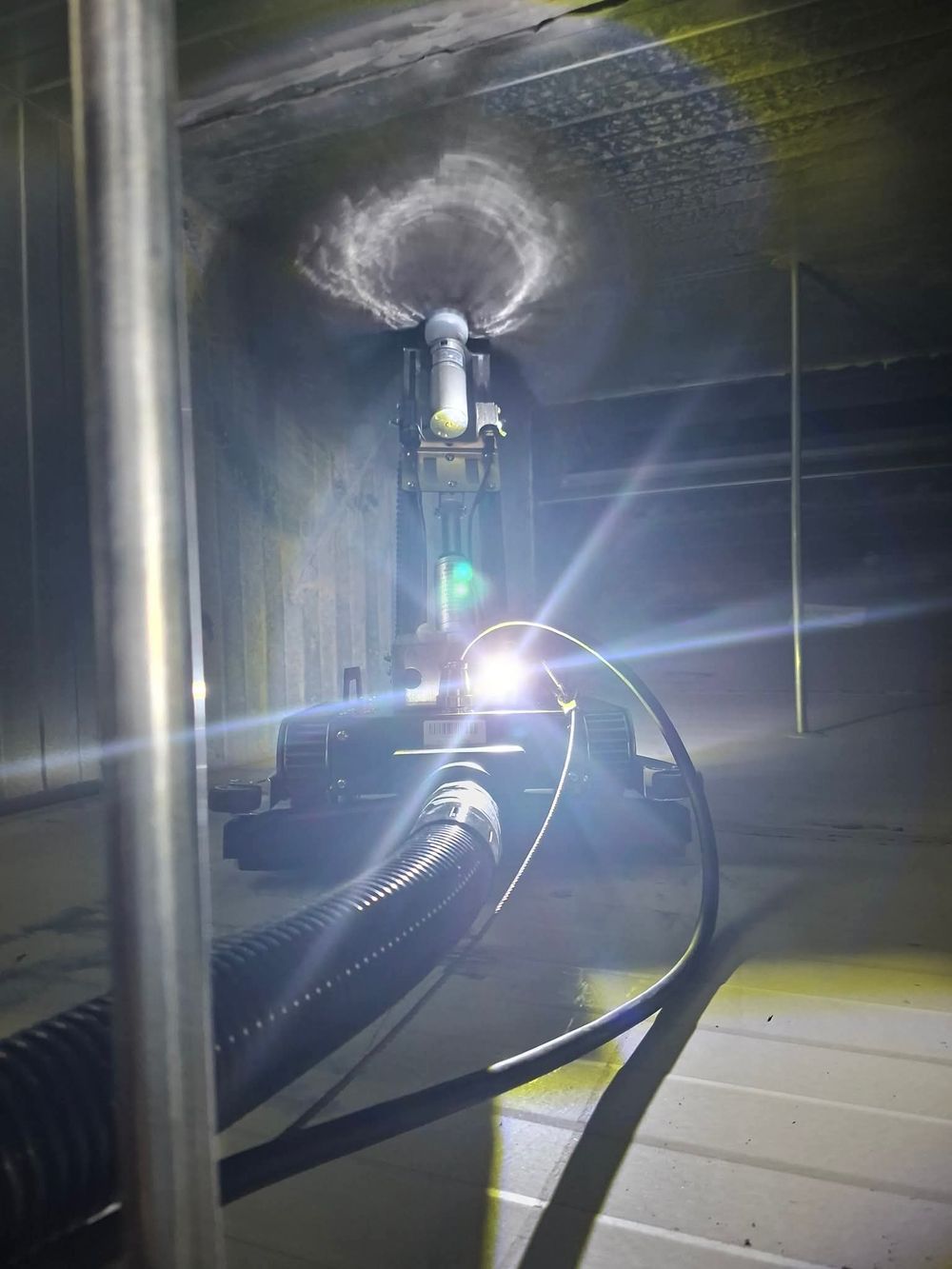 Industrial duct cleaning equipment with bright light illuminating interior of ventilation shaft during maintenance.