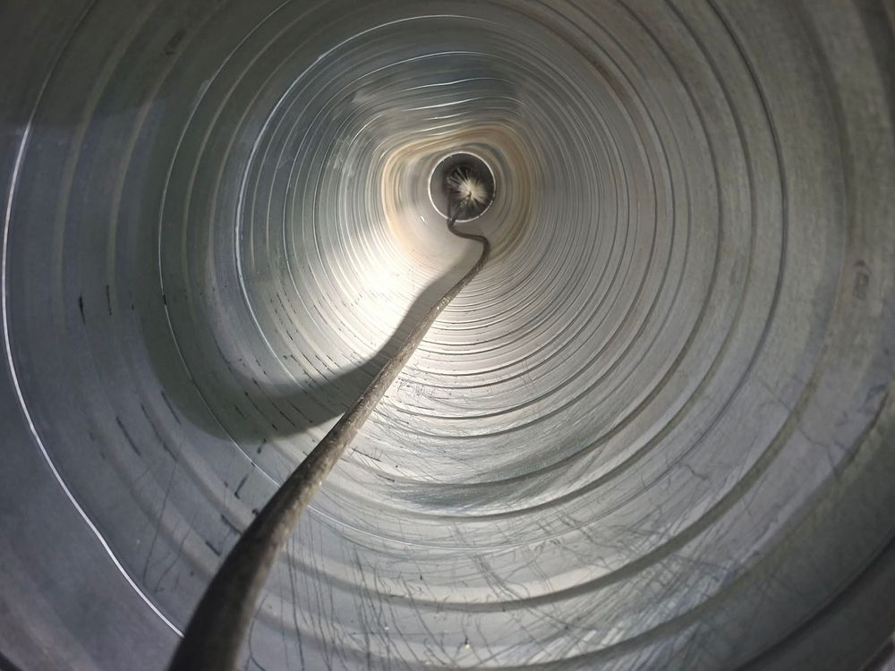 Interior view of a spiral metal duct or tube showing circular ridges converging to a bright center point.