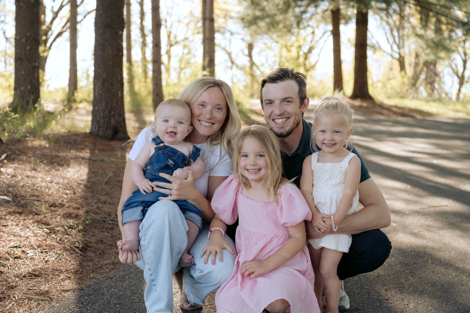 parents and three toddlers smiling and crouching down for a full family lifestyle outdoor spring session in hudson, WI