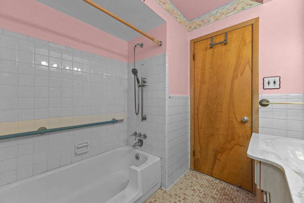Pink bathroom with white subway tile shower, bathtub, wood door, and mosaic floor tiles.