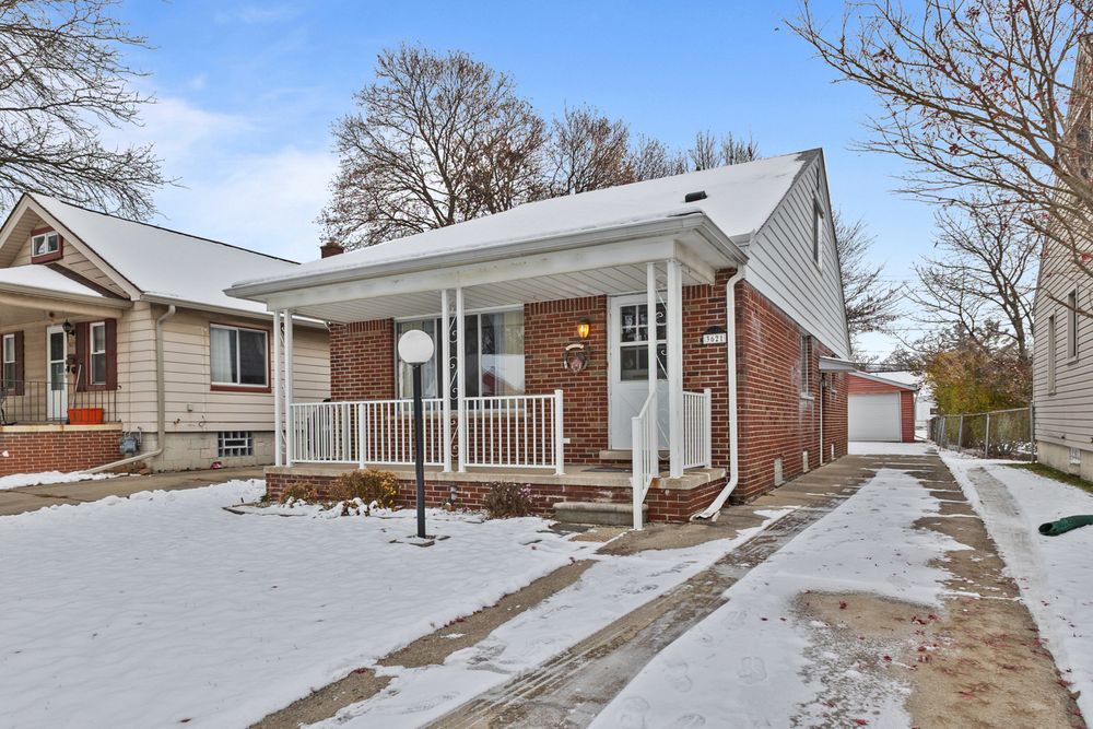Brick bungalow with white porch railings and snowy front yard in winter, detached garage visible on right.