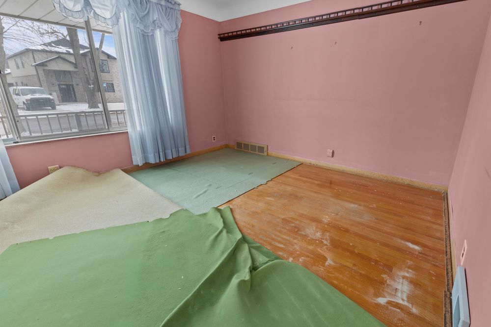 Bedroom with pink walls, hardwood floors partially covered by green underlayment, and a window with blue curtains.