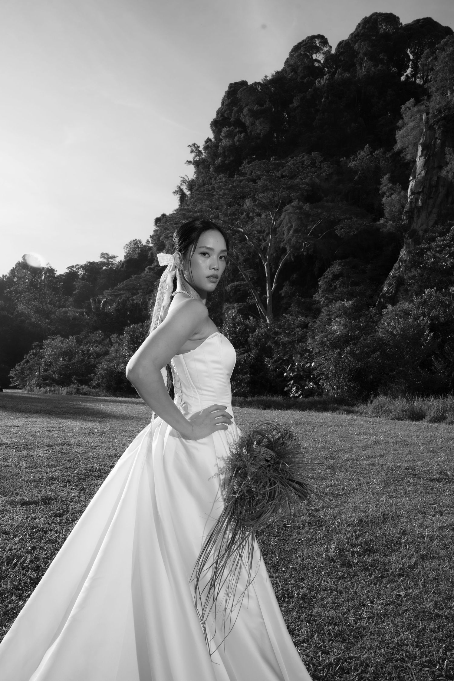Black and white portrait of bride in strapless white gown holding greenery bouquet with rocky hill backdrop.