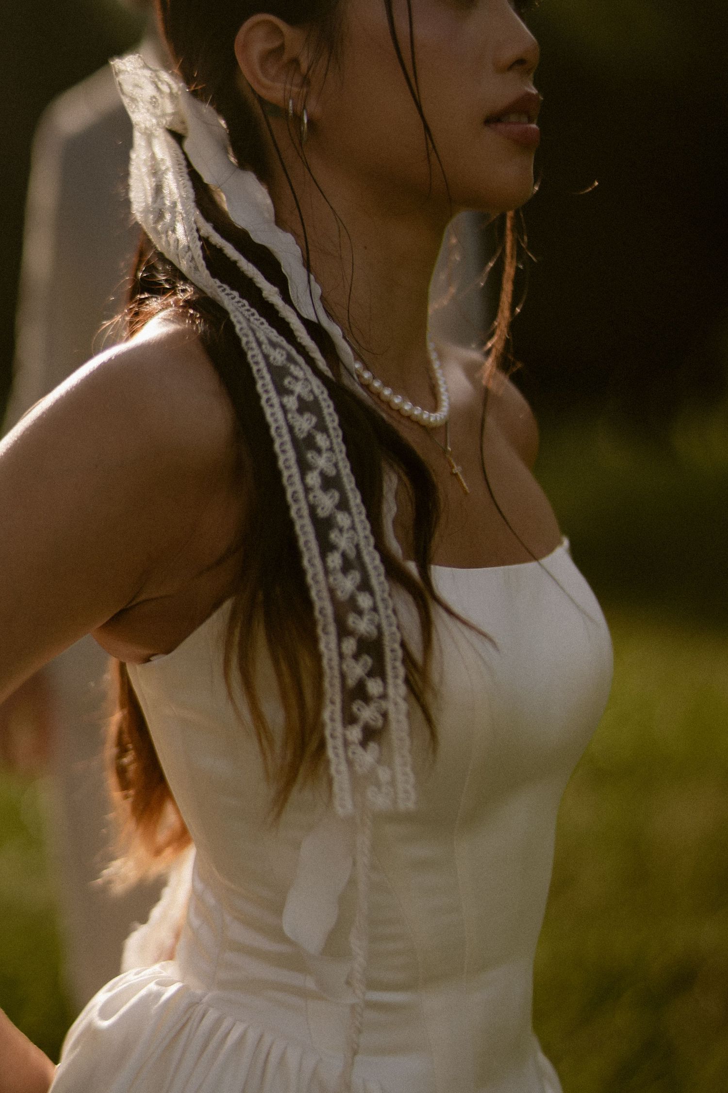 Close-up of bride in white strapless corset gown with lace ribbon and pearl necklace.