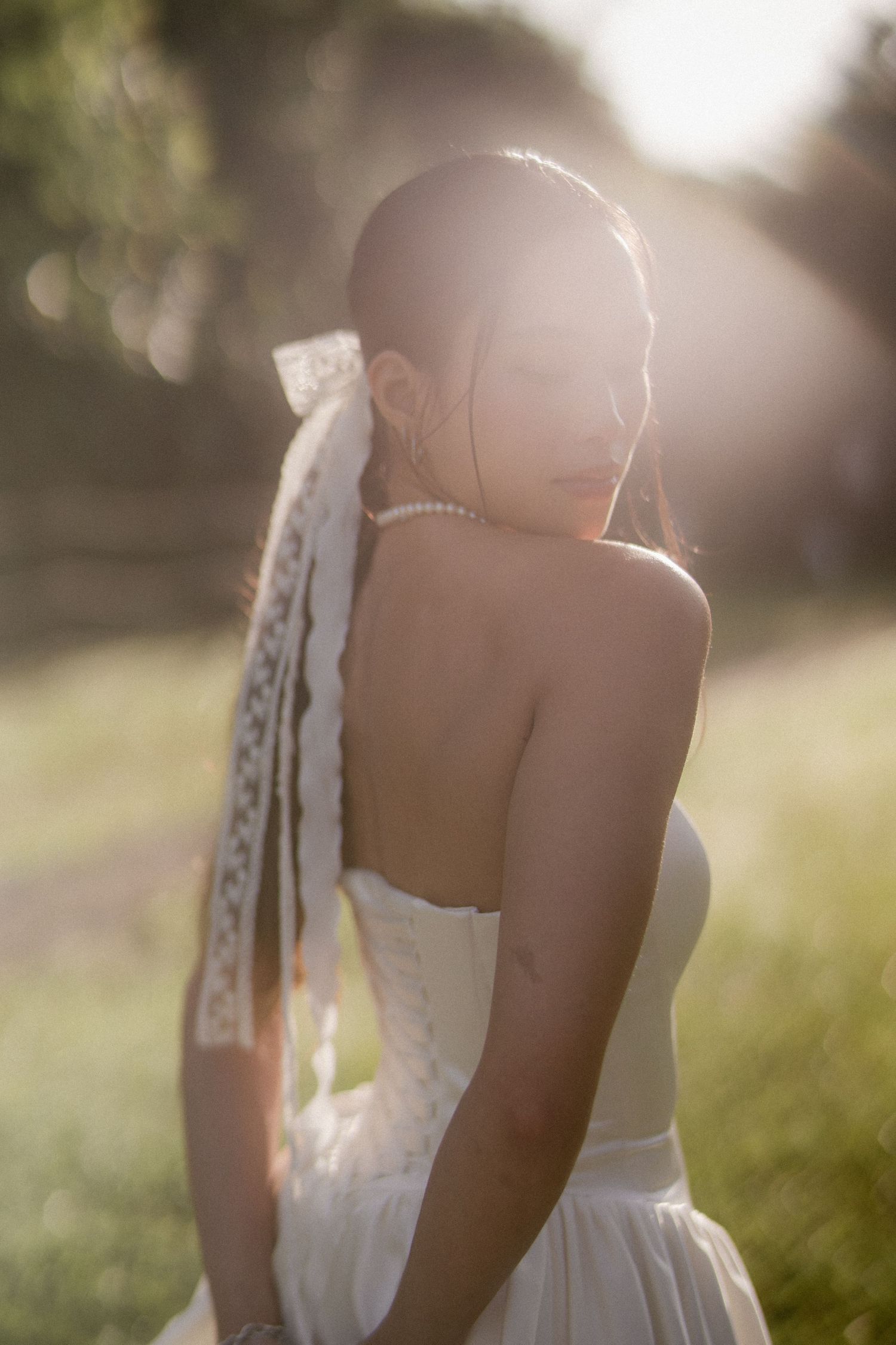 Bride in backless white gown with lace veil glowing in warm sunset light.