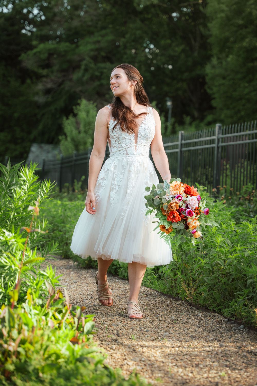 Bride walking along a garden path holding her colorful wedding bouquet at Hartwood Acres.