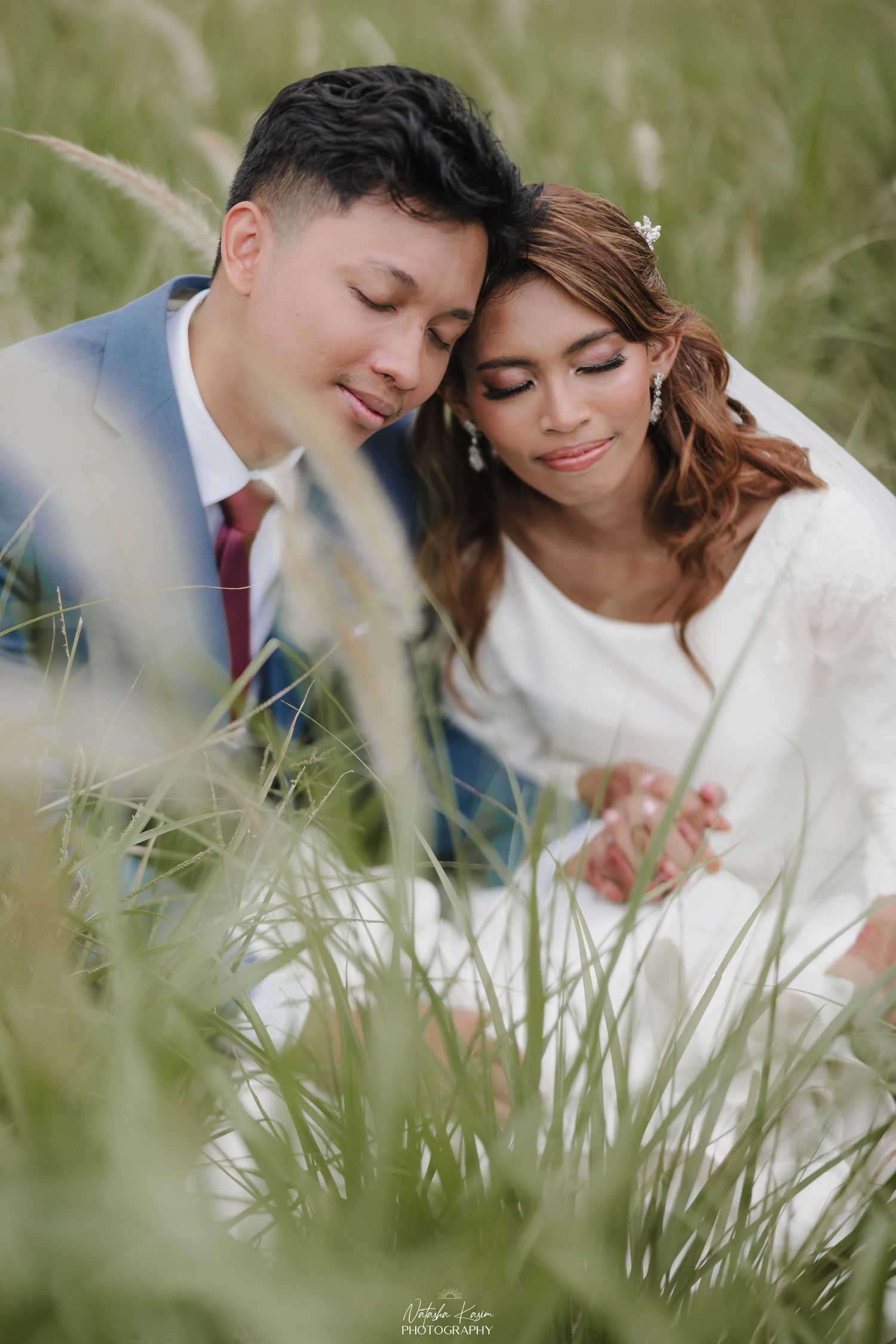 Romantic couple lying in tall grass during outdoor photo session.