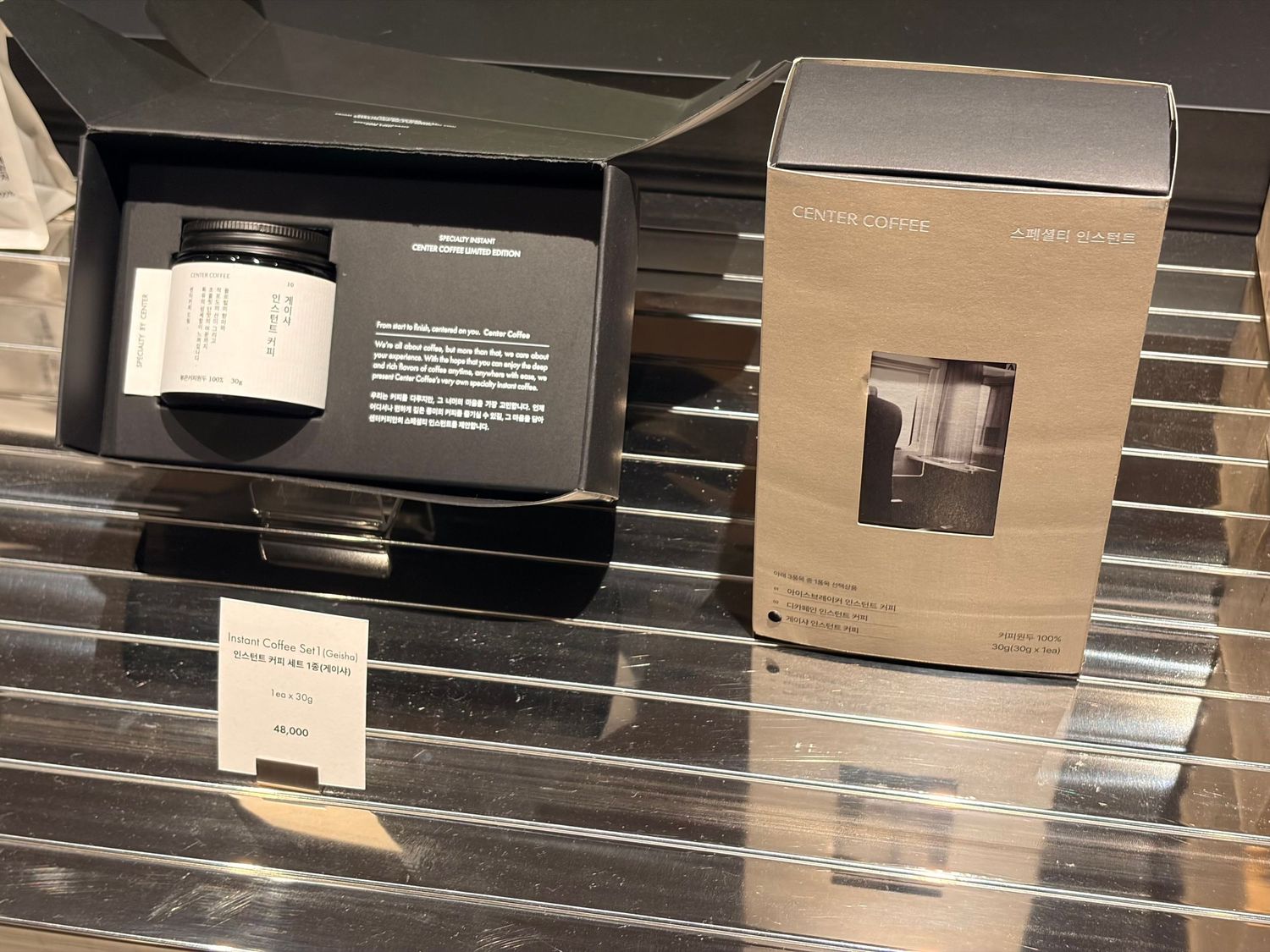Two luxury skincare products in elegant black and white packaging displayed on a reflective surface in a retail store.