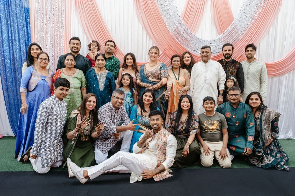 Large Indian family group photo at a festive celebration, wearing colorful traditional attire, posing together indoors.