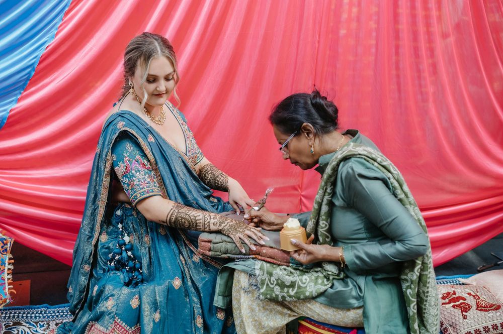 A bride in blue lehenga gets mehndi applied by an artist at a traditional Indian wedding ceremony.