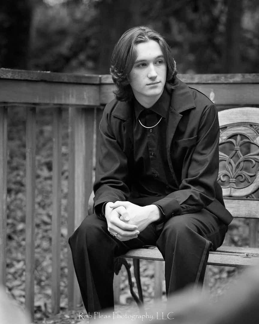 Black and white shot of High school senior male wearing suit while sitting on bench.
