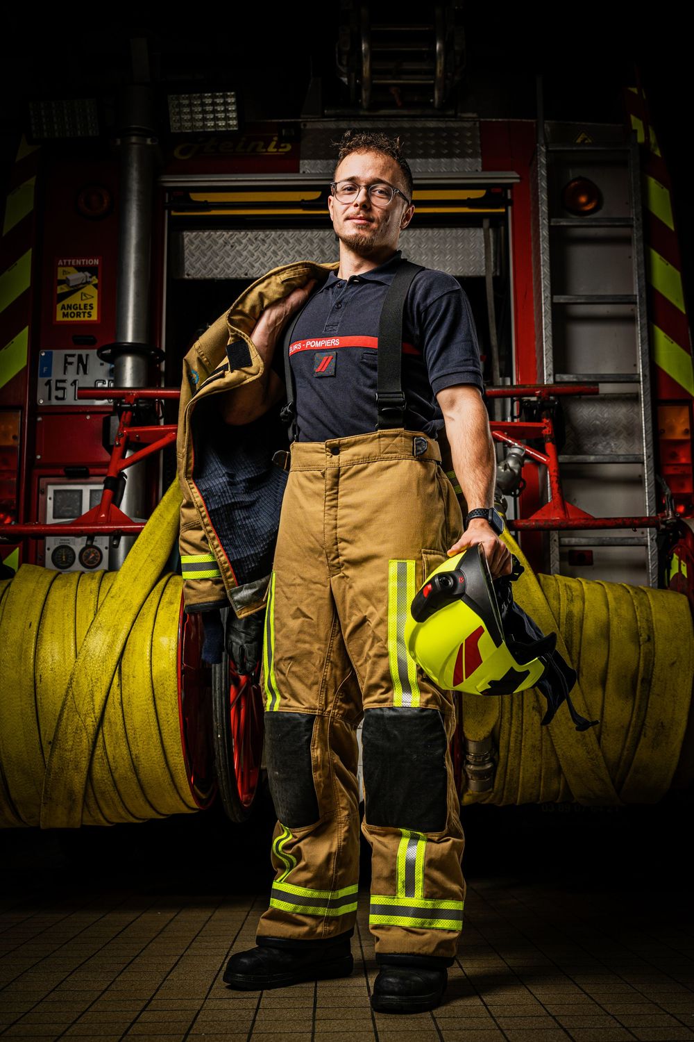 Firefighter in full gear holding a hose and helmet standing in front of a fire truck.