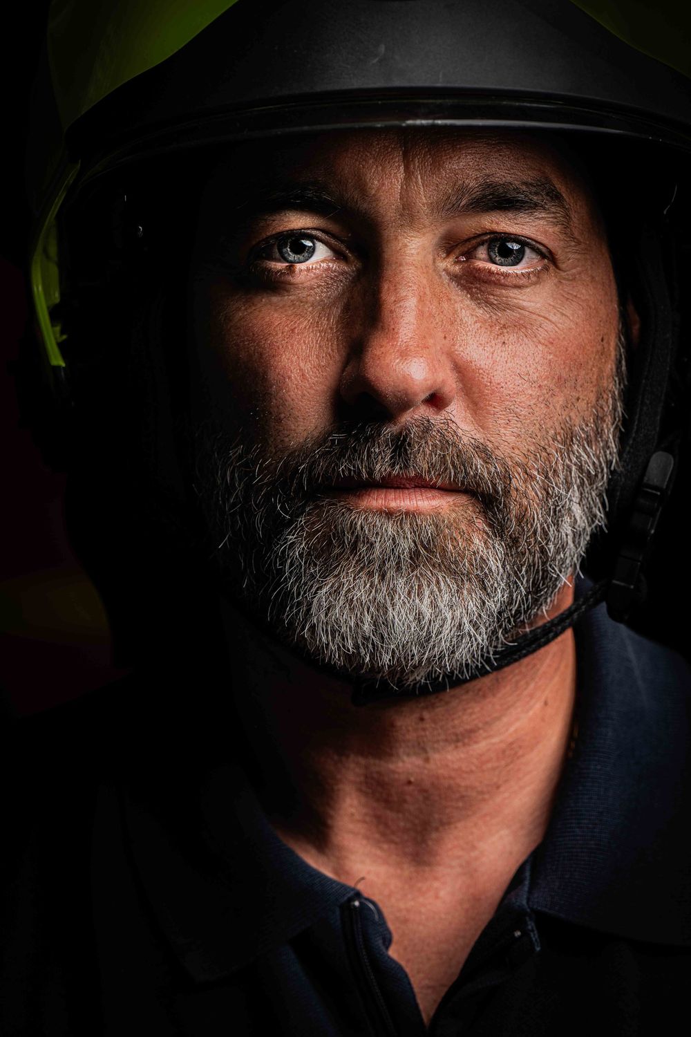 Close-up dramatic portrait of a bearded man wearing a firefighter helmet in dark lighting.